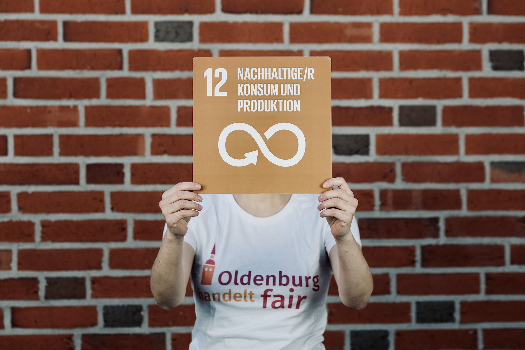 Person im T-Shirt von "Oldenburg handelt fair" mit dem Schild zu SDG 12; Foto: © J. Bädeker