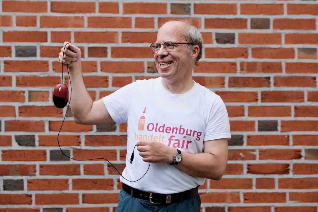 Mann in T-Shirt mit dem Logo von Oldenburg handelt fair und einer Computermaus in den Händen. Foto: © J. Bädeker