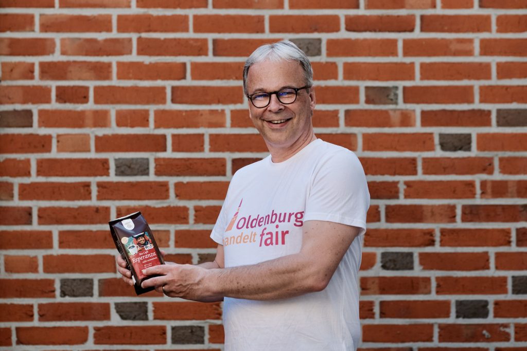 Mann in T-Shirt mit dem Logo von Oldenburg handelt fair und Bio-Kaffee in den Händen. Foto: © J. Bädeker