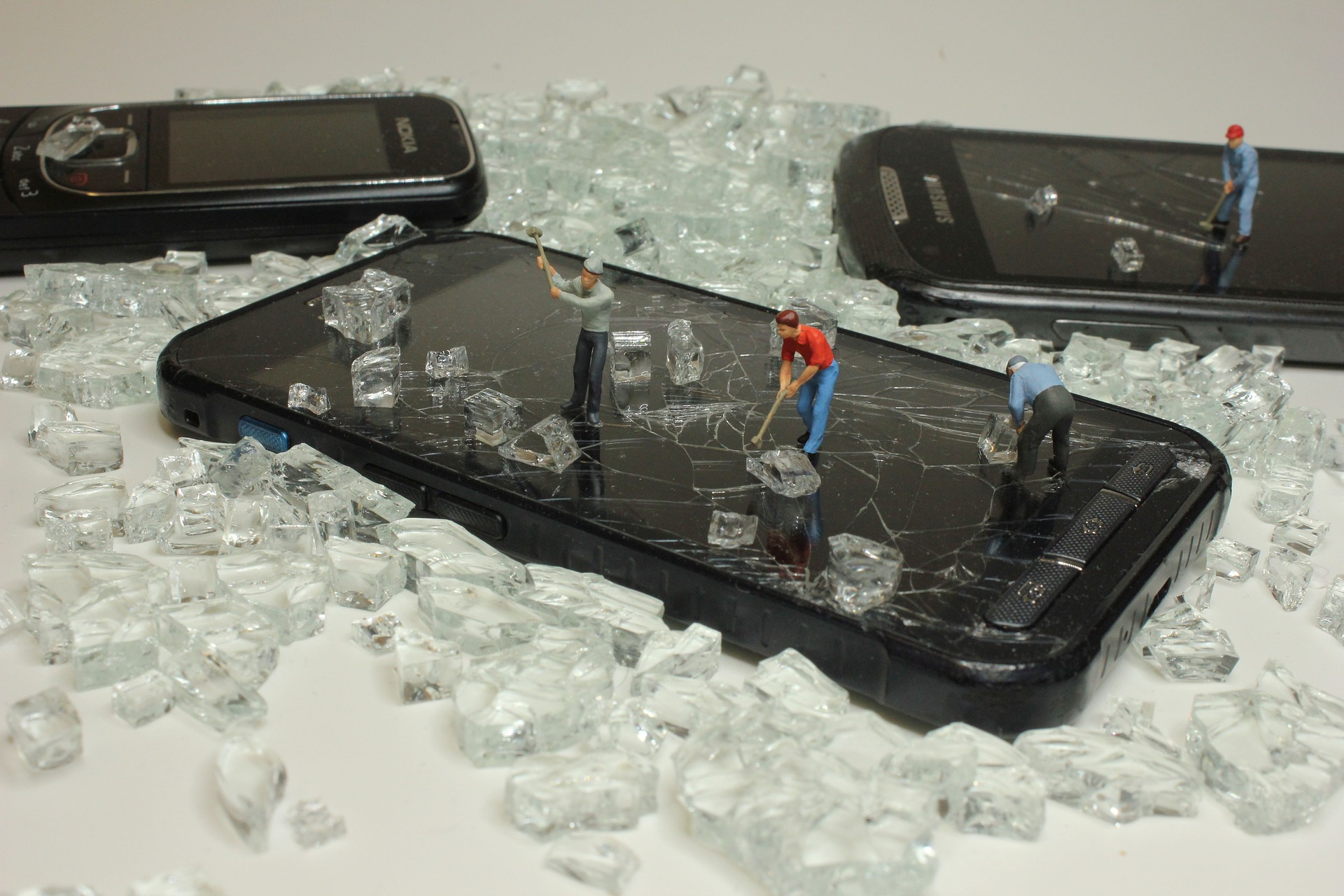Drei Handys liegen inmitten Kristallen, drei kleine Figuren stehen auf einem Smartphone und hämmern.