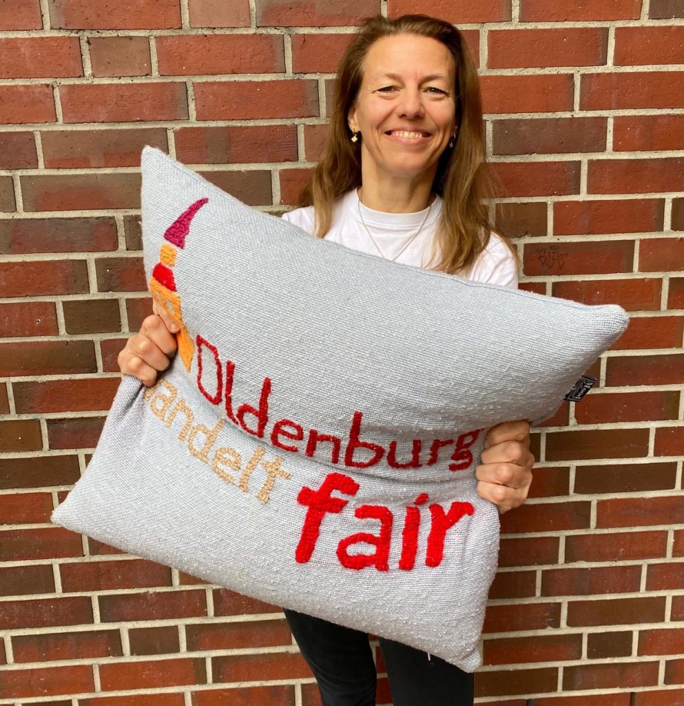 Frau in T-Shirt mit dem Logo von Oldenburg handelt fair und Kissen in den Händen. Foto: © K. Landwehr
