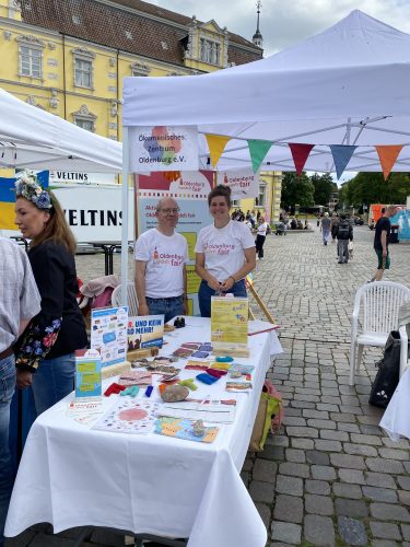 Ein Mann und eine Frau stehen an einem Stand der voller Informationen über Fairen Handel ist.